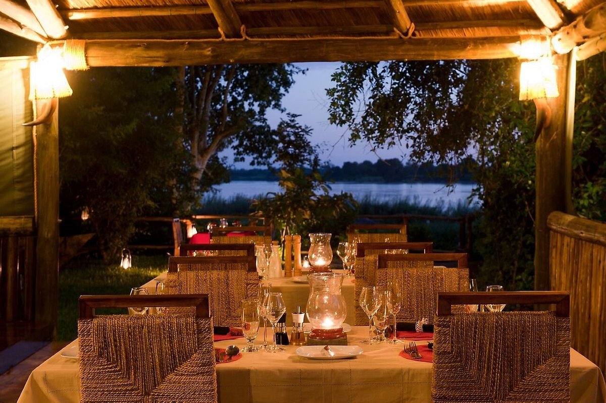 Esstisch am Ufer gedeckt zum Abendessen in der Dämmerung der Selous Kinga Lodge