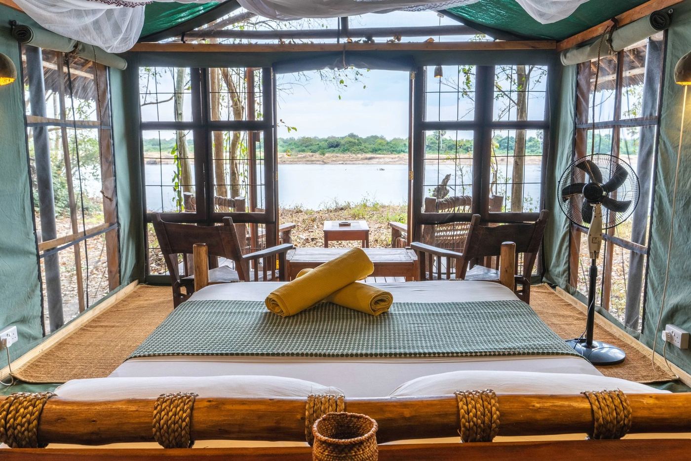 Salon aux parois vitrées surplombant la rivière avec des lits de jour jumeaux au Selous River Camp