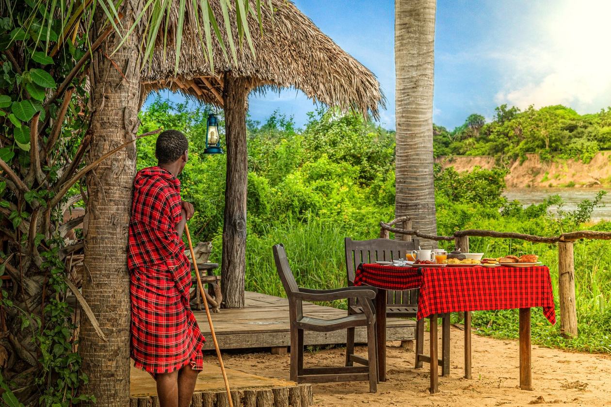 Speistisch am Flussufer unter strohdachtem Unterstand im Selous Wilderness Camp