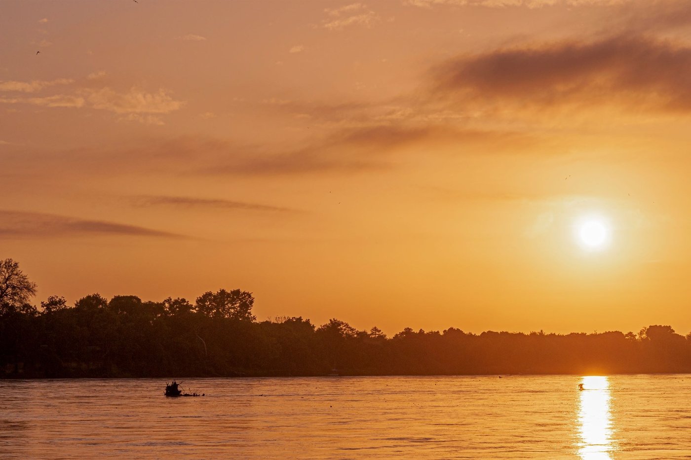 Sonnenuntergang über dem Rufiji-Fluss mit kleinem Boot im Selous Wilderness Camp