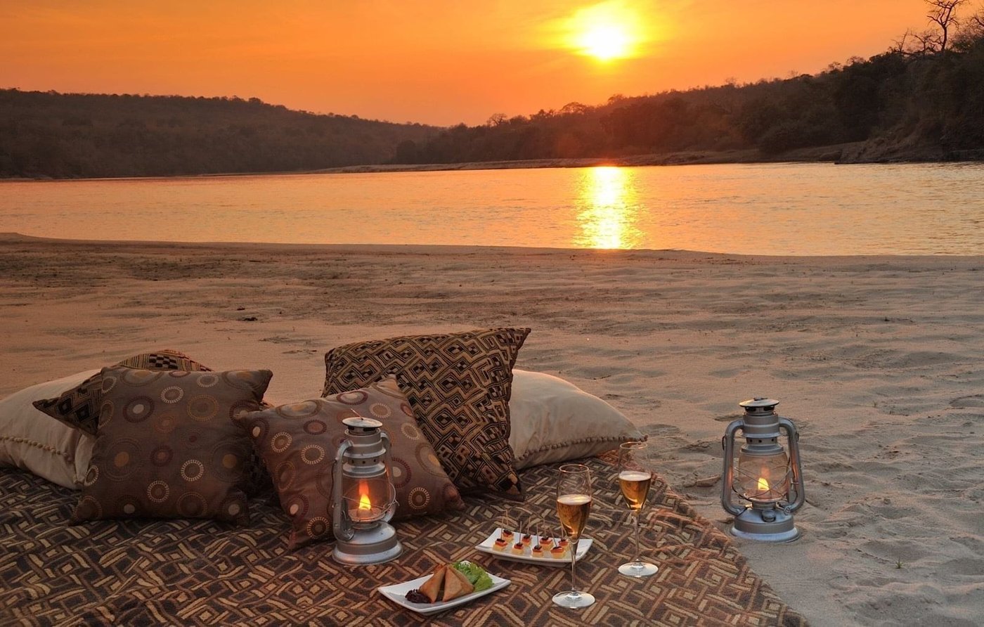 Dîner sur un banc de sable avec coussins et lanternes au coucher du soleil au Serena Mivumo River Lodge