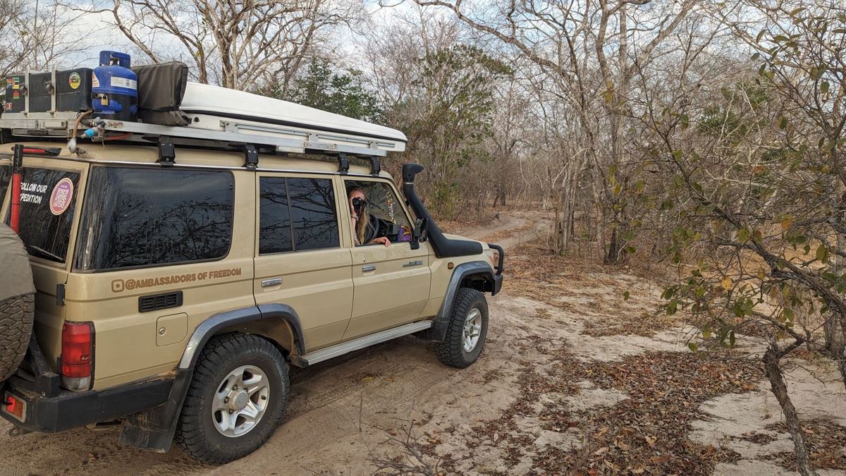 Ein Toyota Land Cruiser mit einem Dachzelt auf einer tiefen Sandpiste in Miombo-Wald